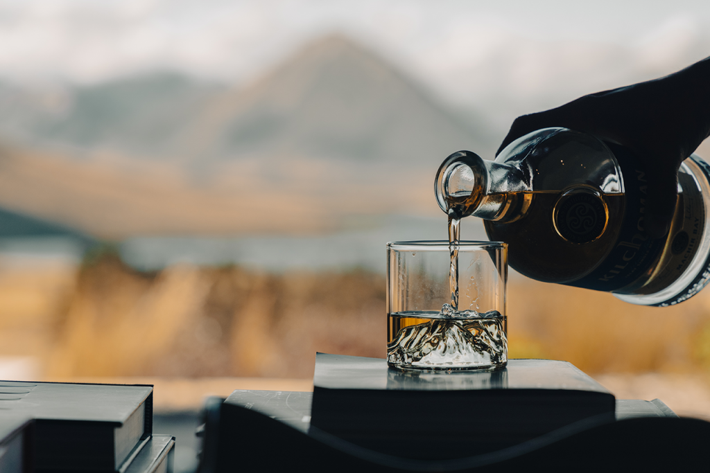 Image of drink being poured in custom glass in foreground, mountains in the background.