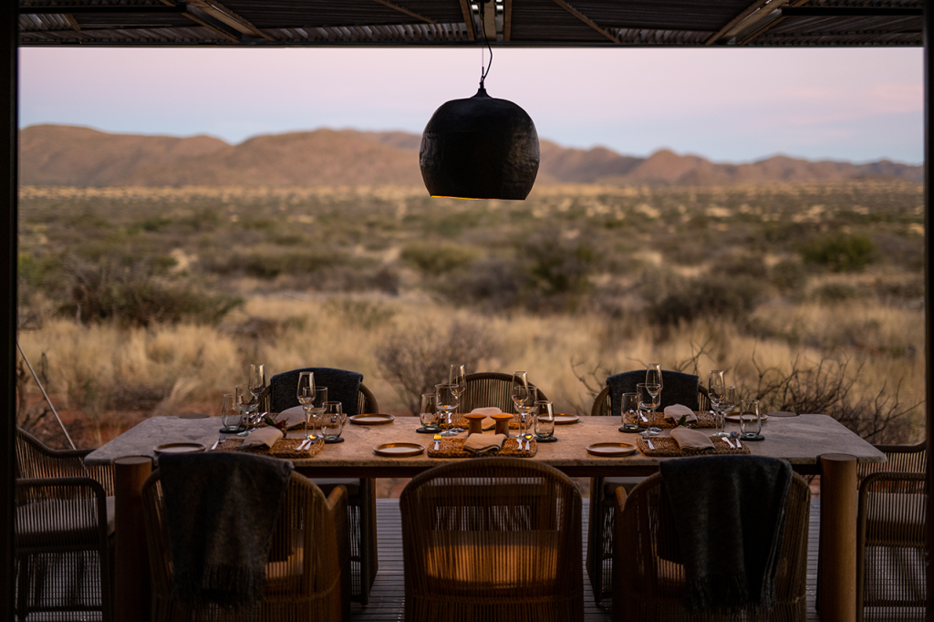 Image with elegant al fresco dining table in the foreground, Kalahari plains in the background.