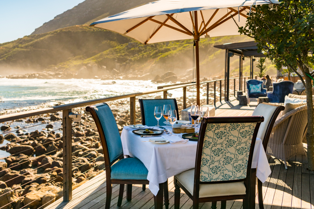 Image of dining table on the deck of Tintswalo Atlantic in the foreground with Hout Bay in the background.