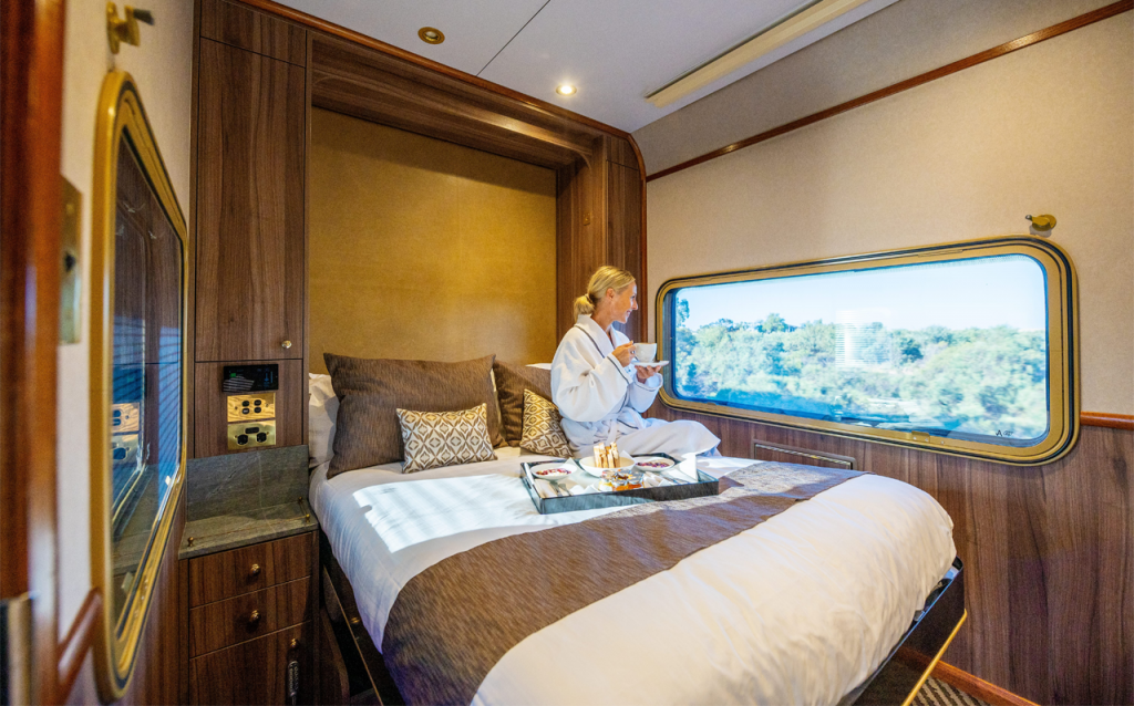 Image of interior suite on The Ghan with woman in bathrobe enjoying the view of the country outside the window.